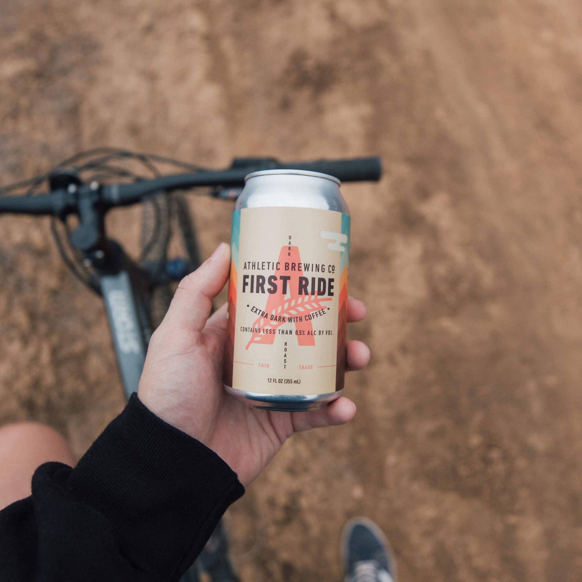 a can offirst ride being held up to the camera in front of a bike on a dirt road