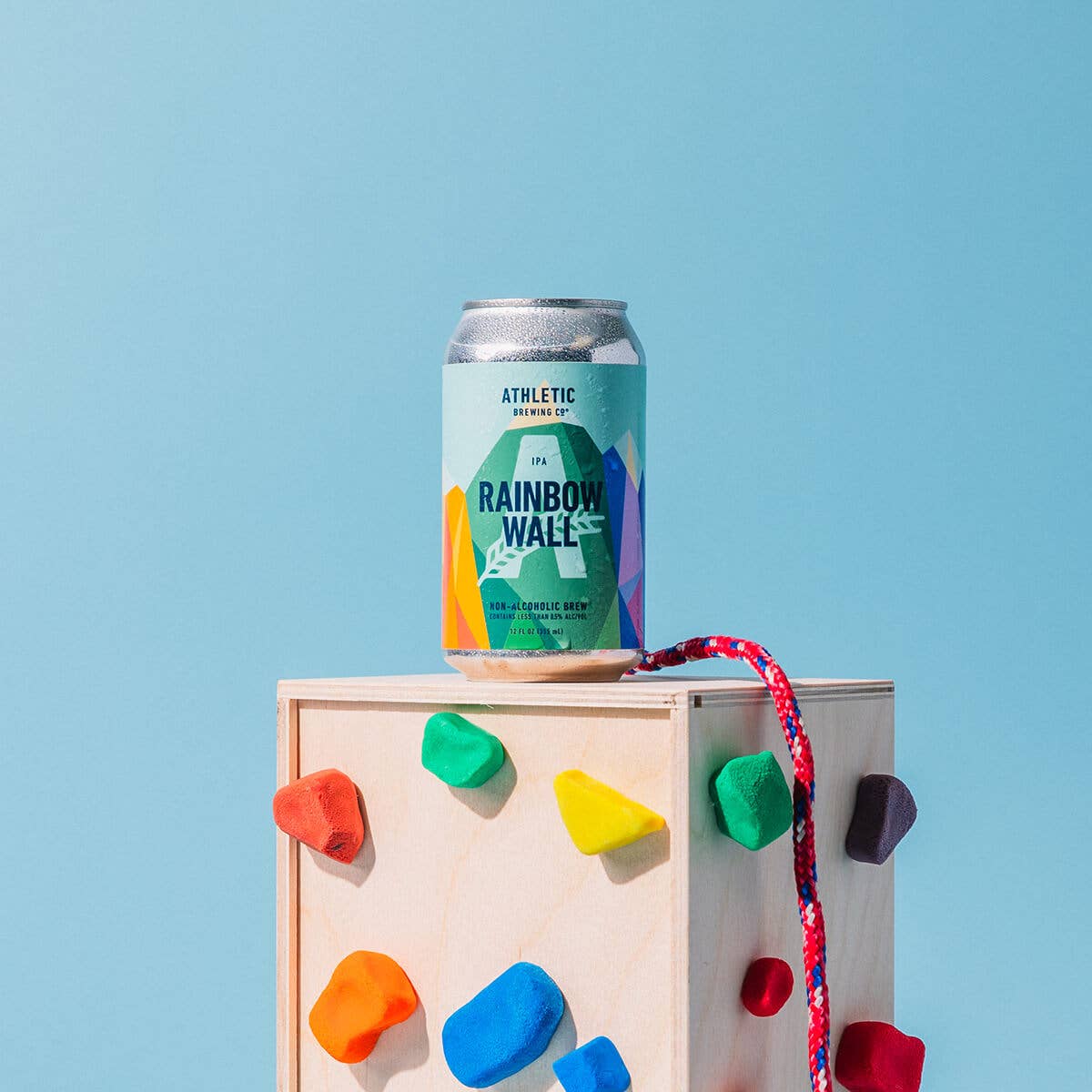 a can of rainbow wall placed on top of a small rock climing wall alongside a rope as if the can itself had climbed the wall.