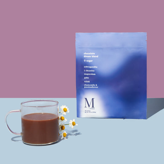 the packaging of moment's chocolate dream blend powder next to a glass with the drink made