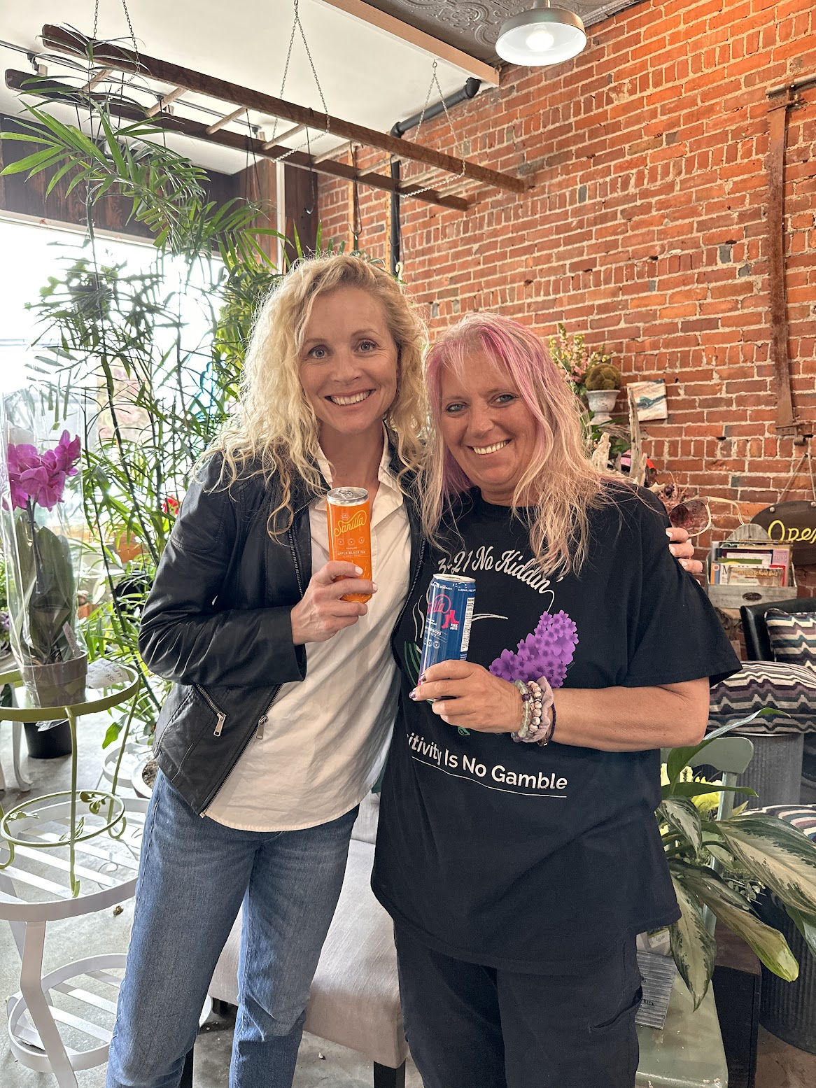 bobbie posing with the founder of sarilla, sara stender delaney in a flowershop. they are both holding cans of sarilla